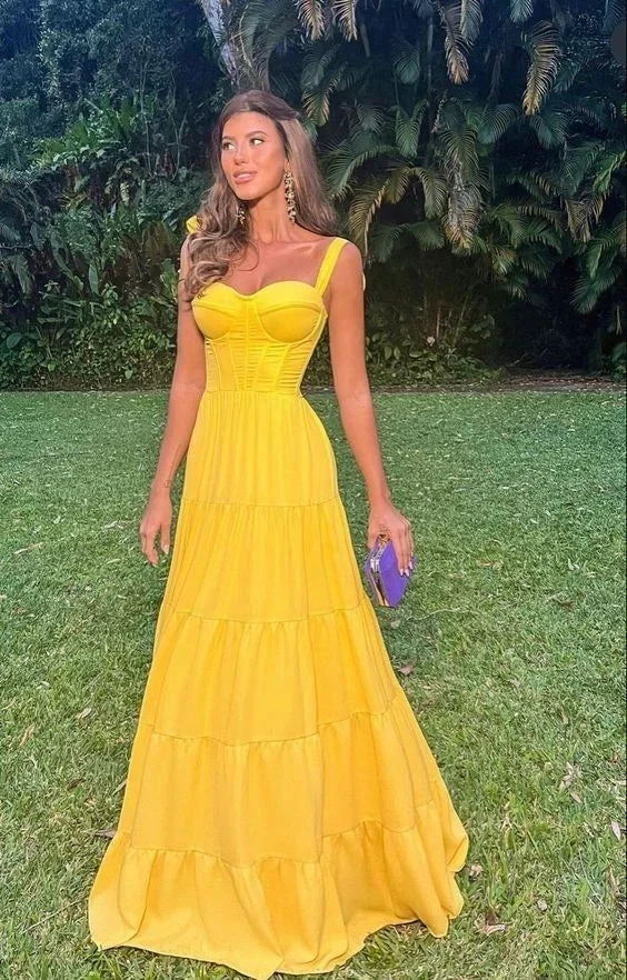 Woman in a vibrant yellow maxi dress with corset bodice, standing outdoors on grass