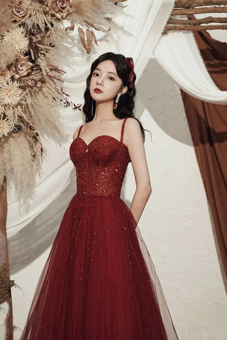 Woman in elegant red sequin evening gown with tulle skirt, standing by floral decor, ZAPDRESS