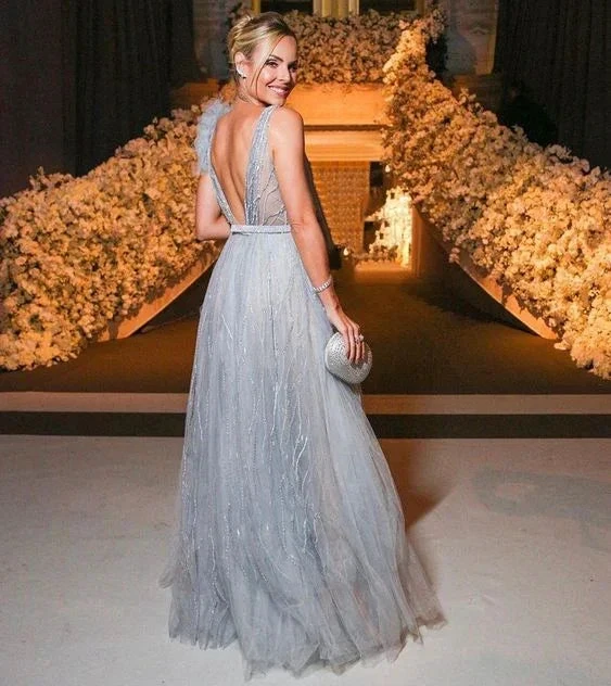 Elegant woman in silver evening gown holding clutch, standing before floral staircase at event