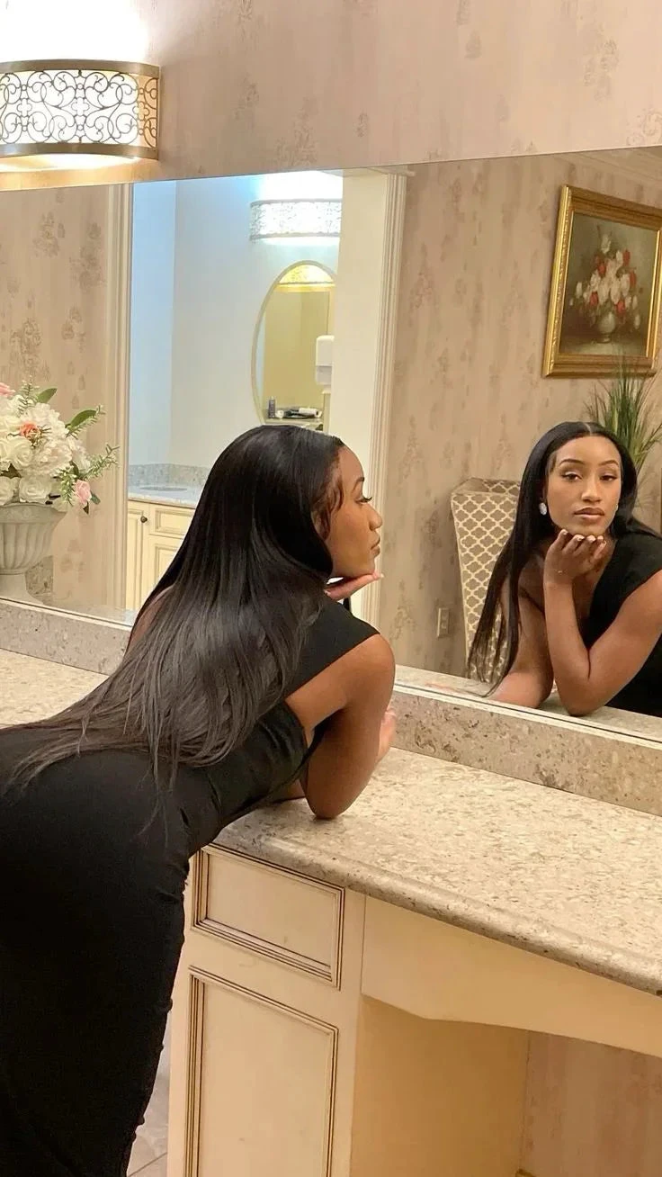 Woman in black dress with long hair posing at a vanity with marble countertop and floral decor