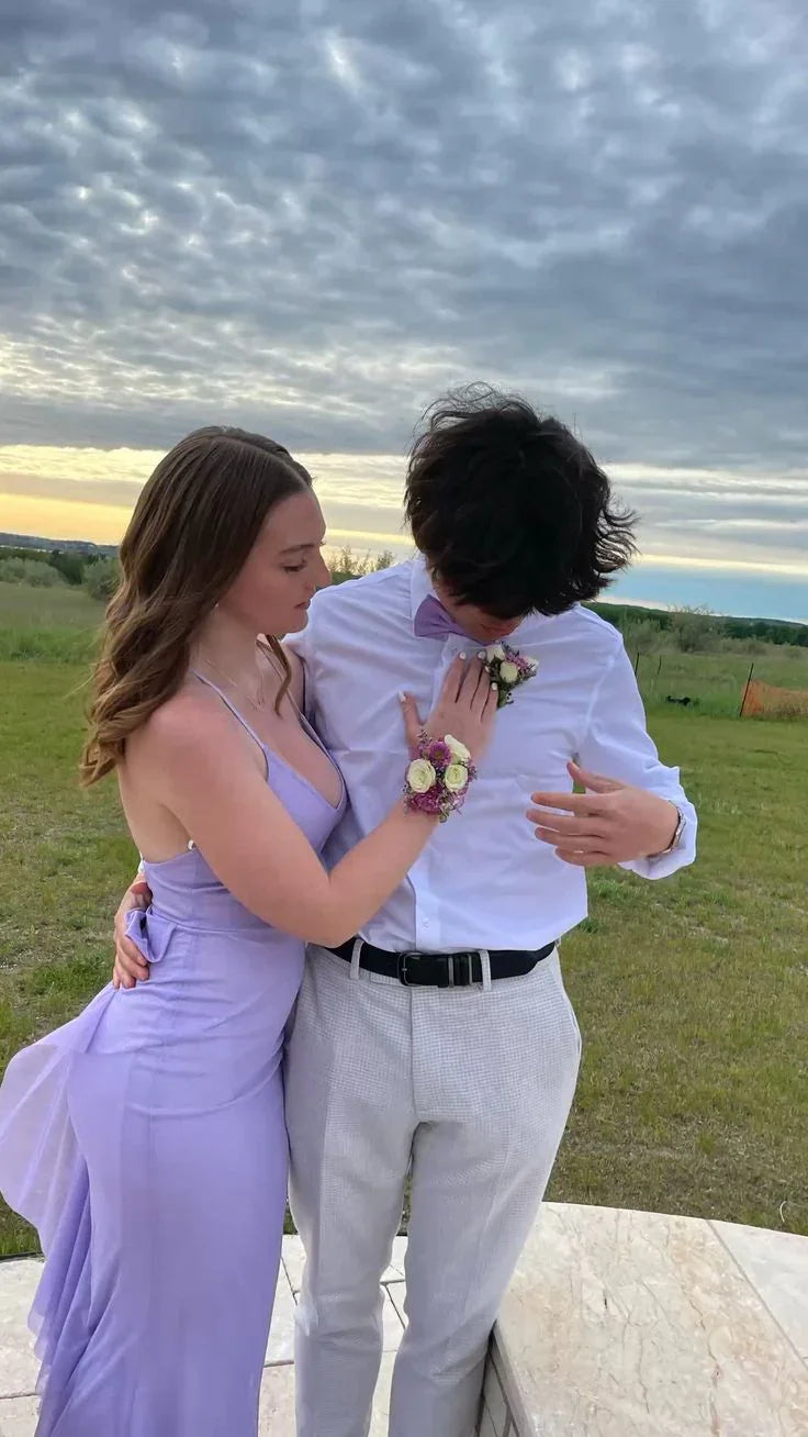 Young couple in formal wear, woman in lavender dress, standing outdoors at sunset