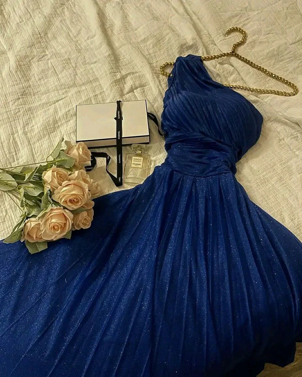 Elegant blue one-shoulder dress with gold chain, roses, and gift box on bed, ZAPDRESS fashion