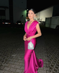 Woman in a vibrant magenta evening gown with a silver purse, posing outdoors at night