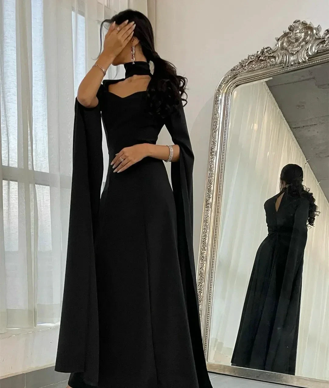 Woman in elegant black evening gown with dramatic sleeves posing by ornate mirror, ZAPDRESS