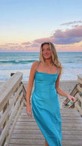 Woman in a blue satin dress on a wooden boardwalk by the ocean at sunset, ZAPDRESS fashion