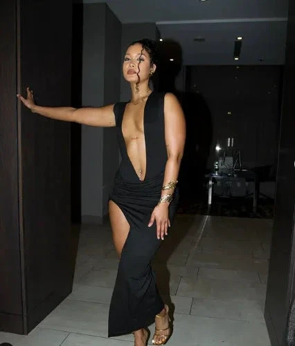 Woman wearing a deep plunge black evening gown from ZAPDRESS, standing in modern hallway