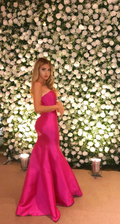 Woman in bright pink evening gown posing by white rose flower wall at ZAPDRESS event