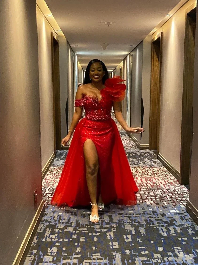 Woman in vibrant red evening dress with thigh-high slit and floral detail, walking indoors