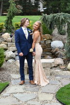 Couple in formal attire, woman in lace gown, man in blue suit, standing in garden near rocks