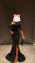 Elegant woman in black off-shoulder evening gown with a slit, holding a clutch, ZAPDRESS fashion