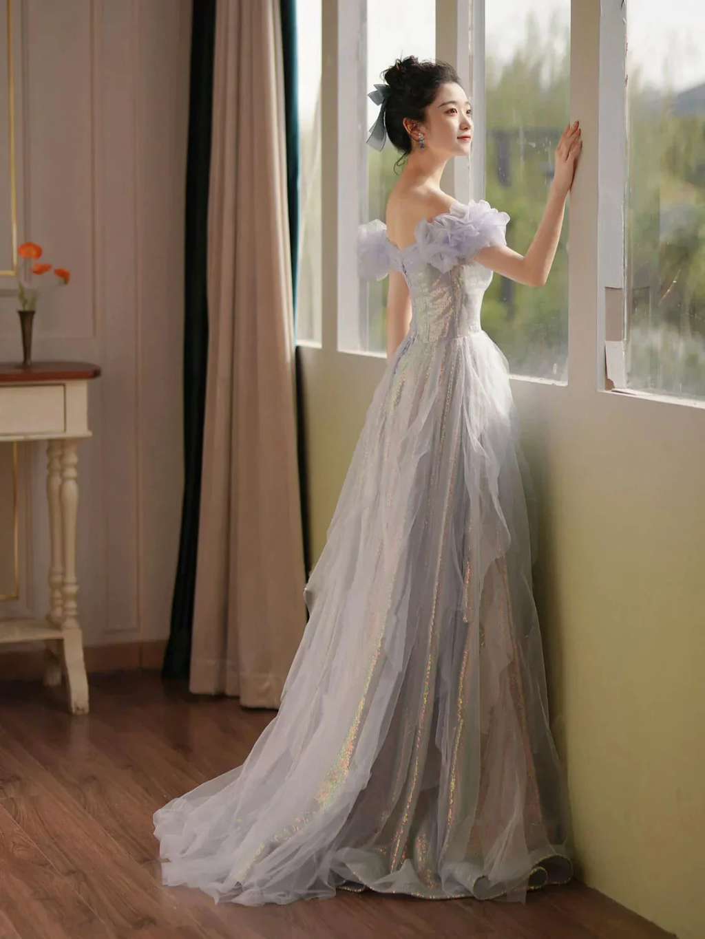 Woman in iridescent off-shoulder evening gown standing by window, ZAPDRESS fashion