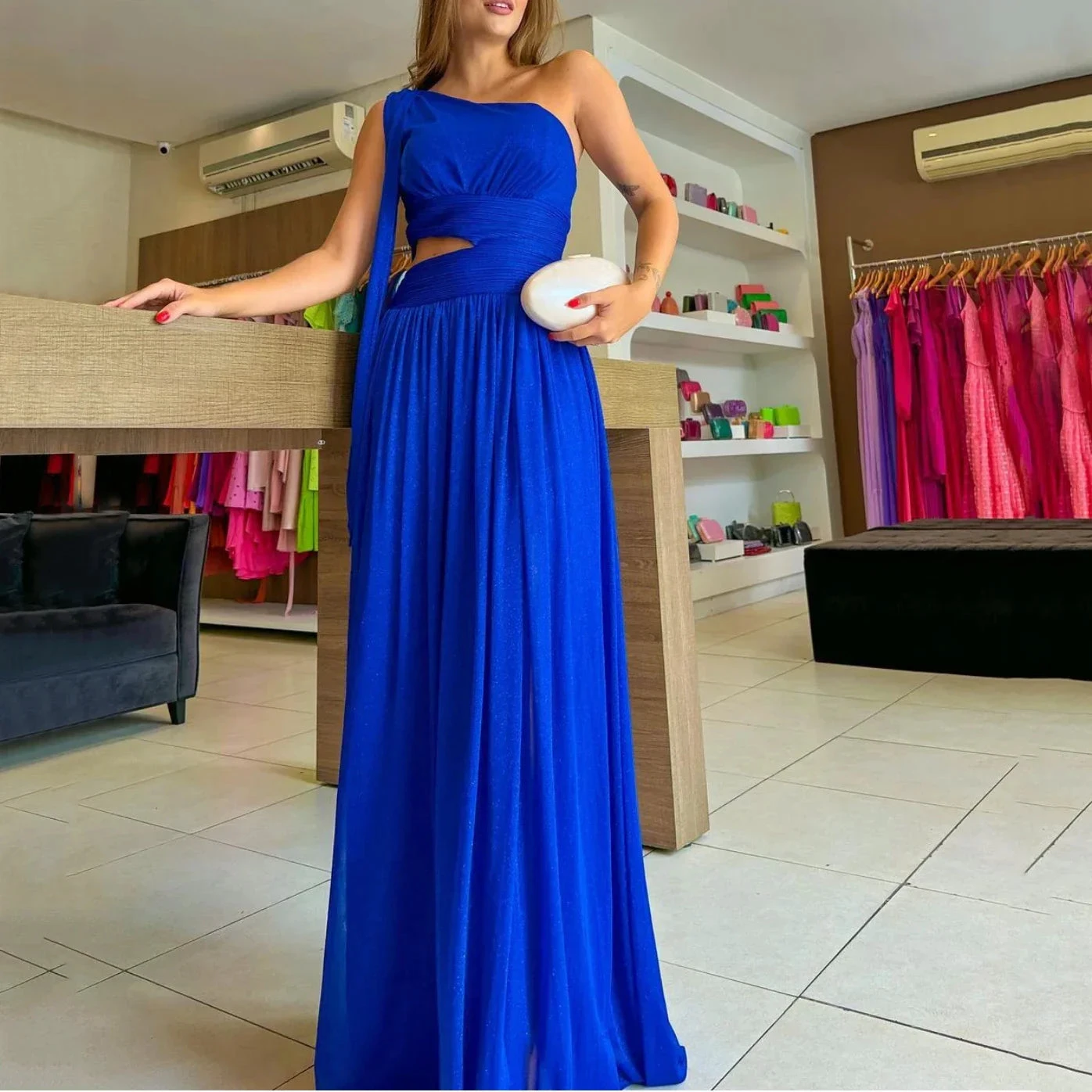 Woman in a vibrant blue evening gown at ZAPDRESS boutique, holding a white clutch.