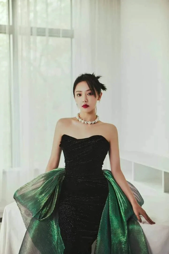 Woman wearing elegant strapless black gown with green accents in bright modern room, ZAPDRESS