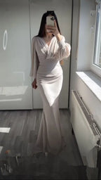 Woman wearing a long, elegant light beige gown from ZAPDRESS, posing indoors by a window.