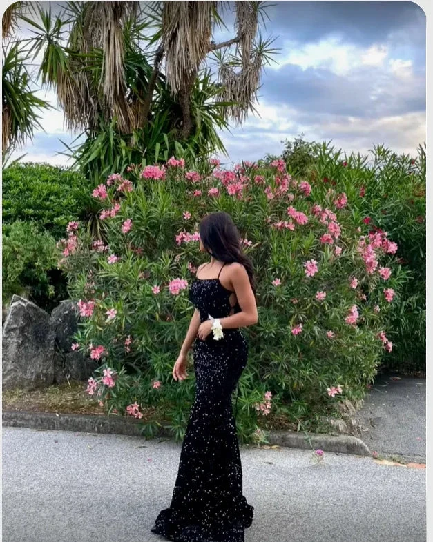 Woman in a sparkly black evening gown standing outdoors near lush pink flowering bushes, ZAPDRESS