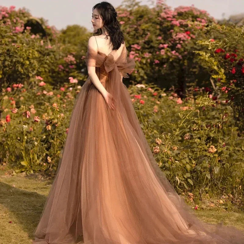 Woman in flowing brown tulle dress with bow stands in rose garden, ZAPDRESS fashion