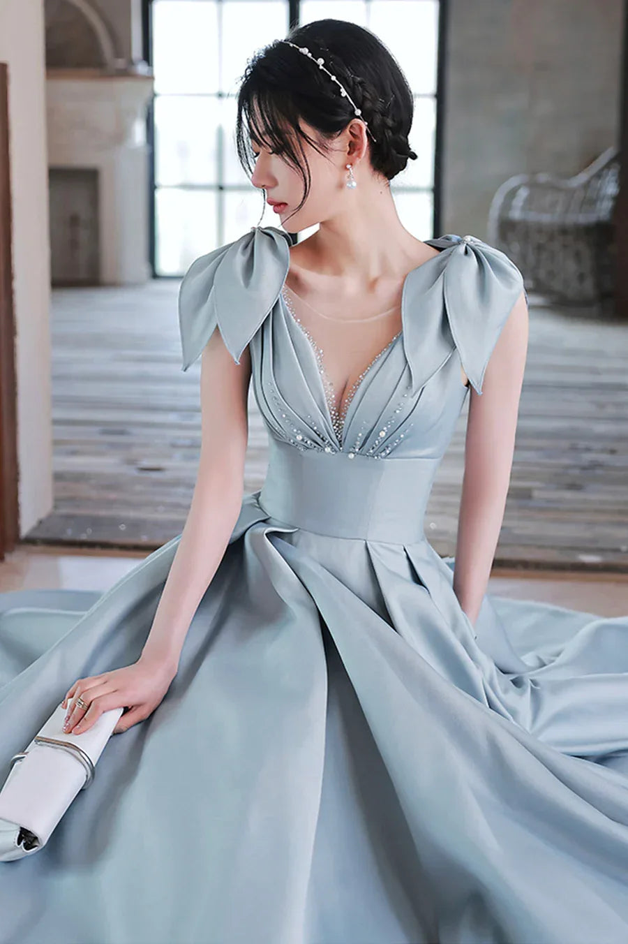 Elegant woman in light blue formal gown with floral shoulders, sitting indoors, ZAPDRESS fashion