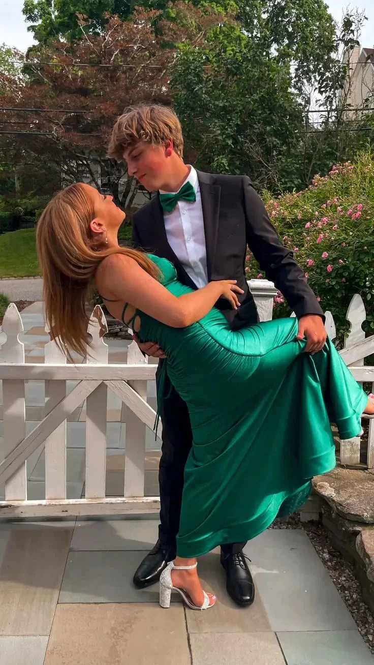 Young couple in formal wear, woman in emerald green dress, outdoors by white fence, ZAPDRESS style