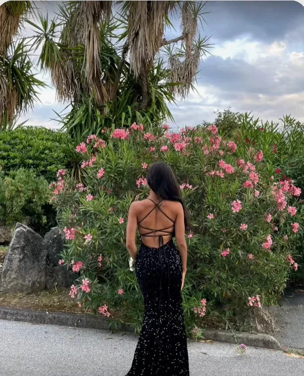 Woman in black sequin evening dress with strappy back by pink flowering bush, ZAPDRESS fashion